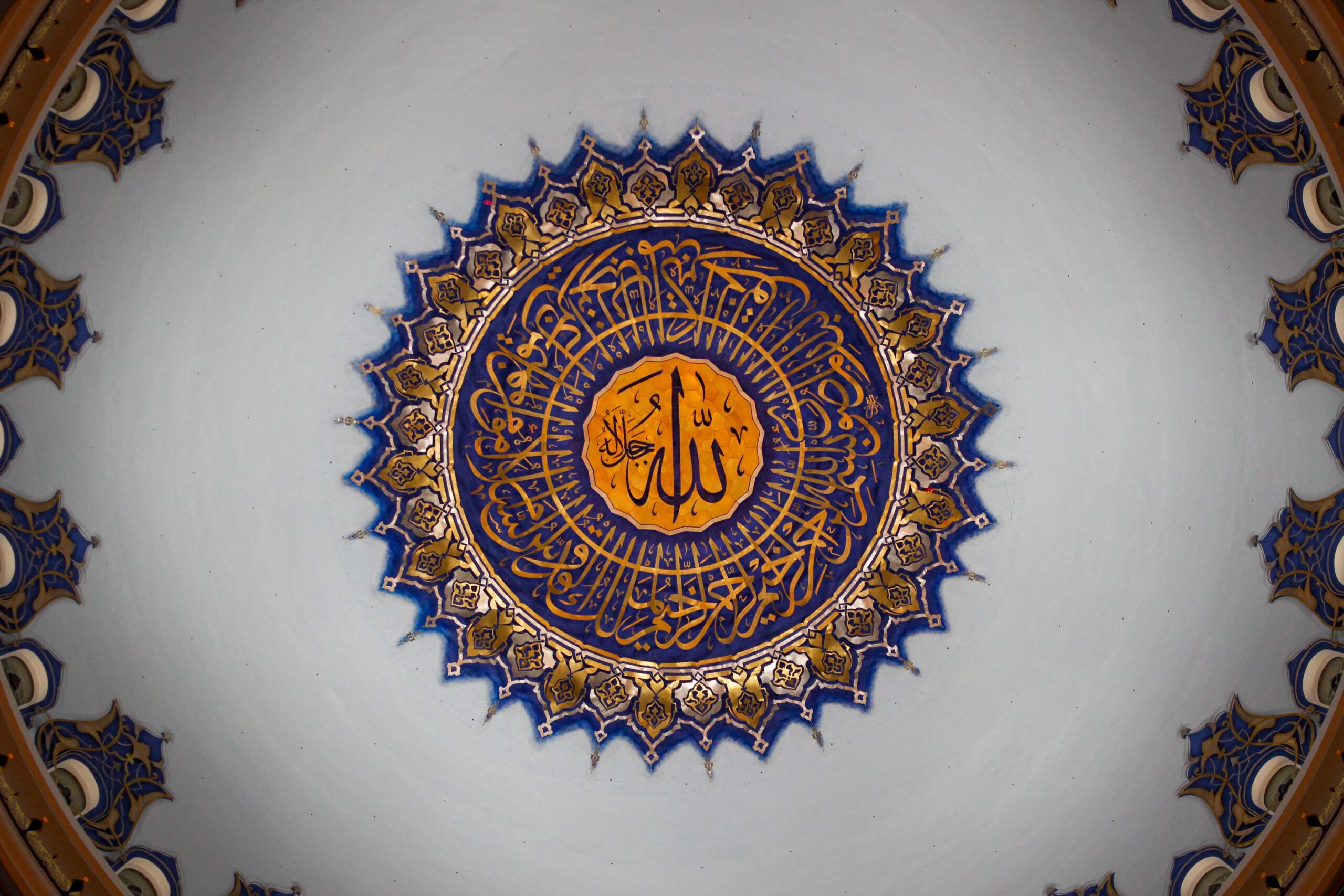 Detailed view of a beautifully decorated mosque dome ceiling in İstanbul, showcasing Islamic art and Arabic calligraphy.