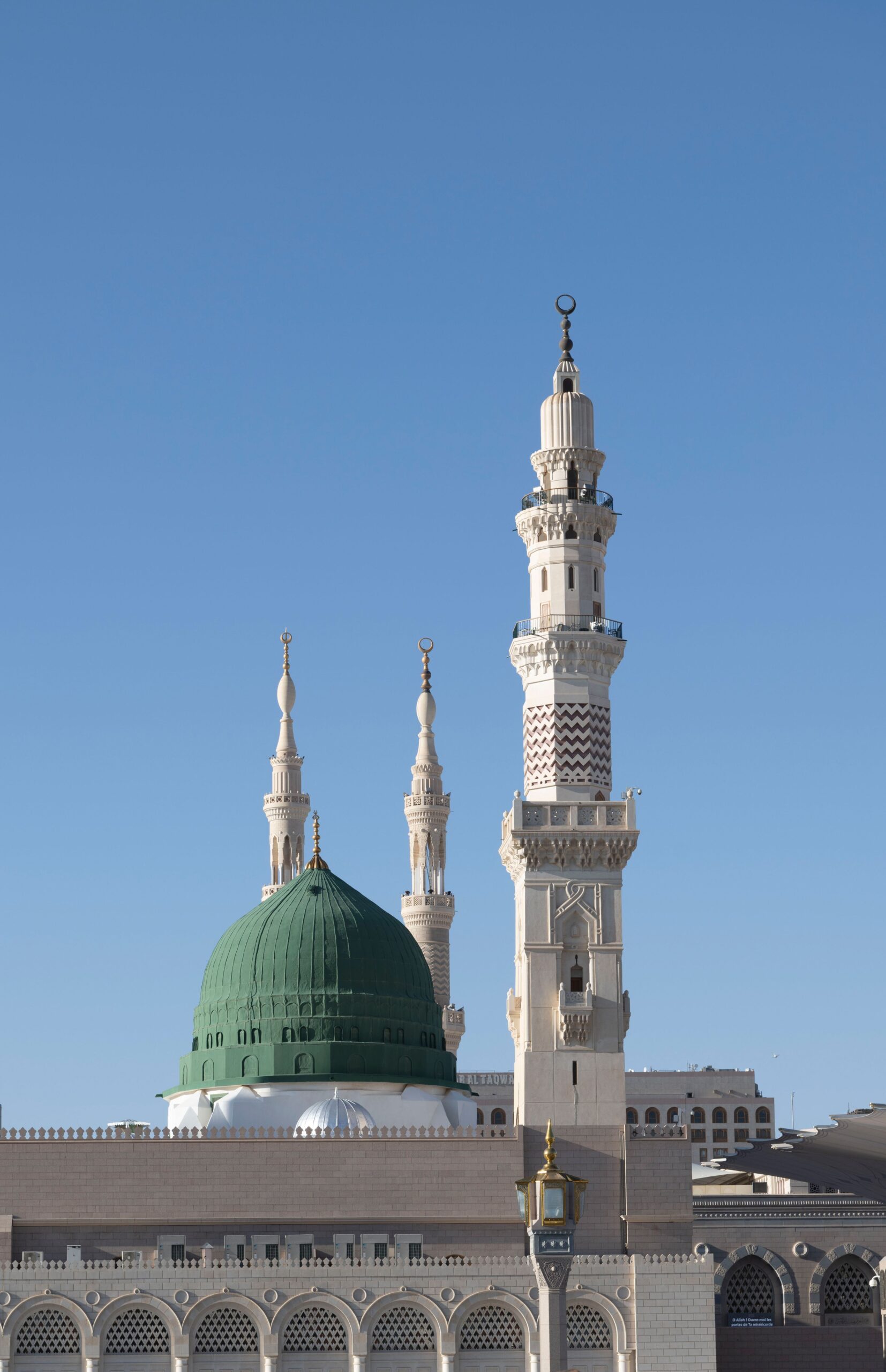 View of the Green Dome and minarets of Al-Masjid an-Nabawi in Medina, Saudi Arabia under clear blue skies.